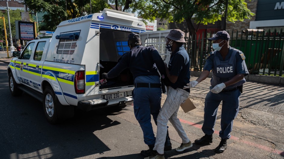 South African Police Service (SAPS) officers leads a man to the back of a police vehicle in Sunnyside, Pretoria.