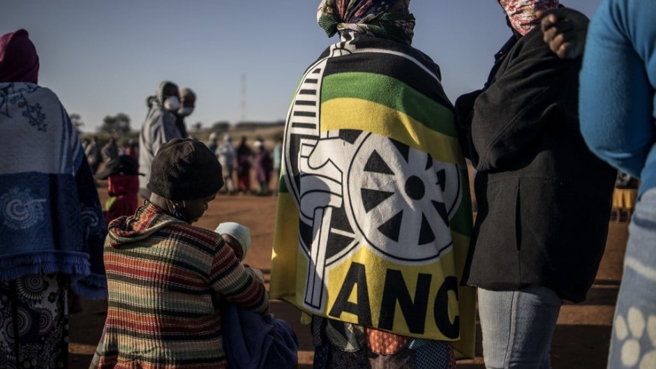 A woman wearing a blanket printed with the logo of South African ruling party African National Congress (ANC) queues with residents at a football field in the early morning during a distribution of hampers, masks, soap and sanitiser organised by different charities at the Iterileng informal settlement near Laudium, Pretoria, on May 20, 2020.