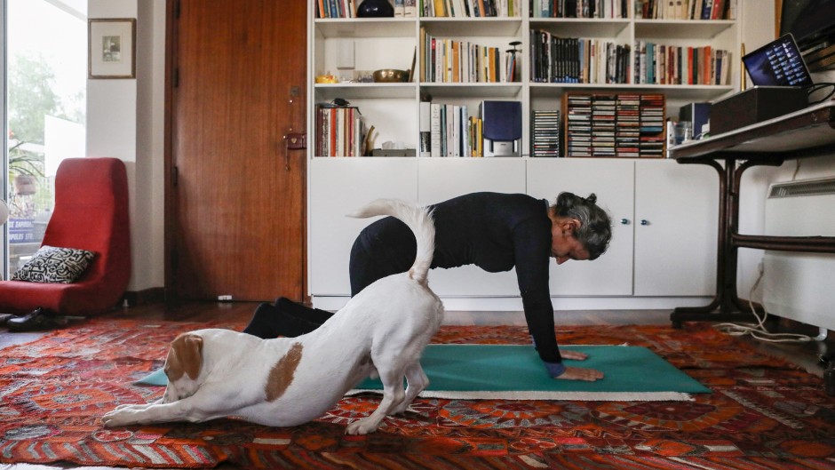 Thanks to an online pilates course, a Cypriot woman exercises at home, while her dog stretches too beside her.