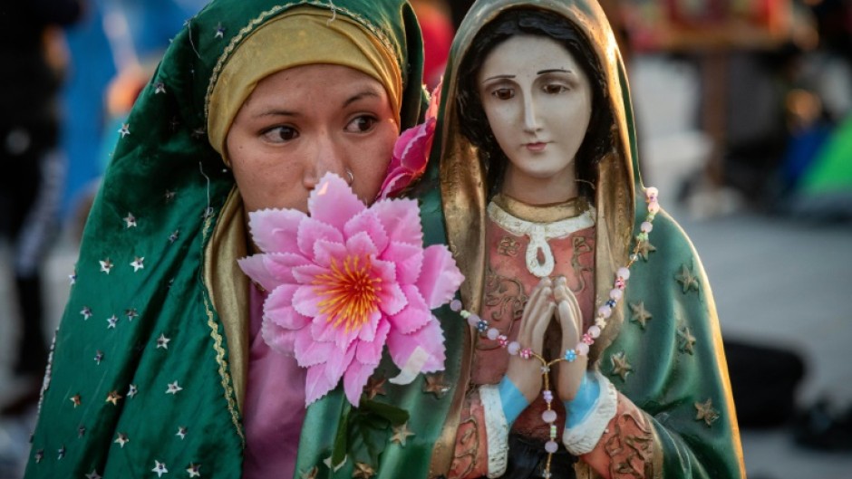 A woman stands next to an image of the Virgin of Guadalupe outside the Guadalupe basilica in Mexico, December 12 2022