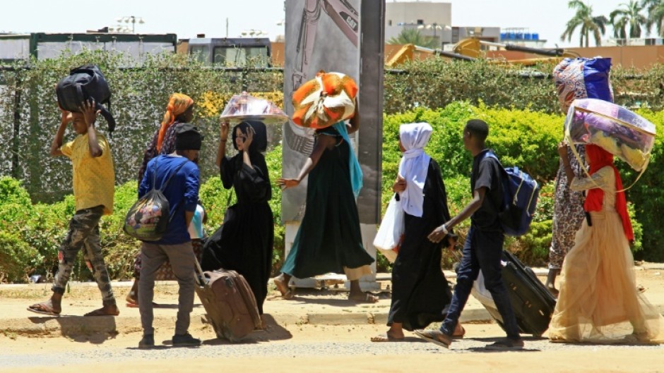 People carrying their belongings flee on foot along a street in southern Khartoum on April 18