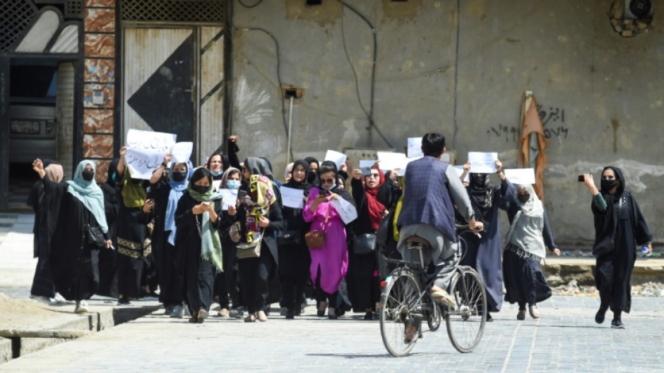 Afghan burqa-clad women walk past a Taliban security personnel along a street in Jalalabad, Afghanistan