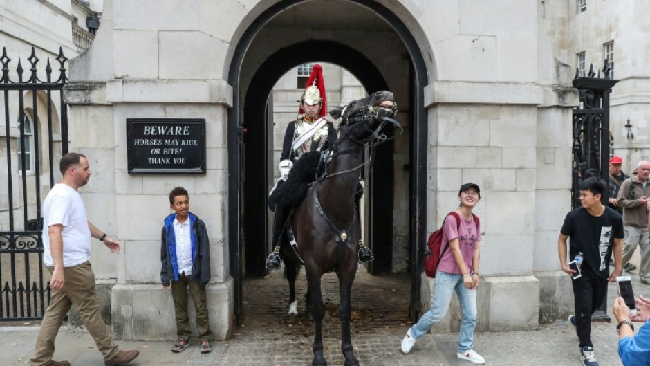 Tourists stand next to a member of The Life Guards squadron at Horse Guards in central London