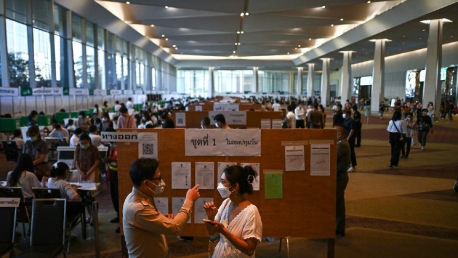 A voter (R) asks for directions to cast her ballot at a polling station inside a shopping mall in Bangkok