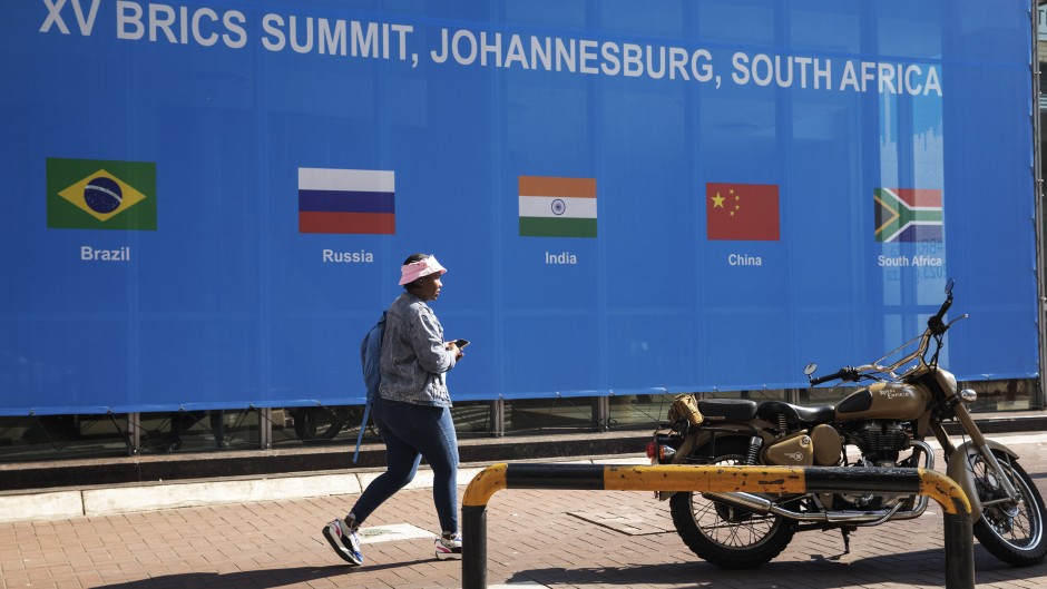 A woman walks past a banner outside the venue for the 2023 BRICS Summit at the Sandton Convention Centre in Sandton, Johannesburg, on August 20, 2023.