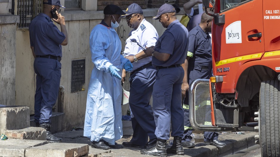 A man wearing forensic clothes speaks to a member of the SAPS at the scene of the deadly blaze in Johannesburg. AFP/Guillem Sartorio