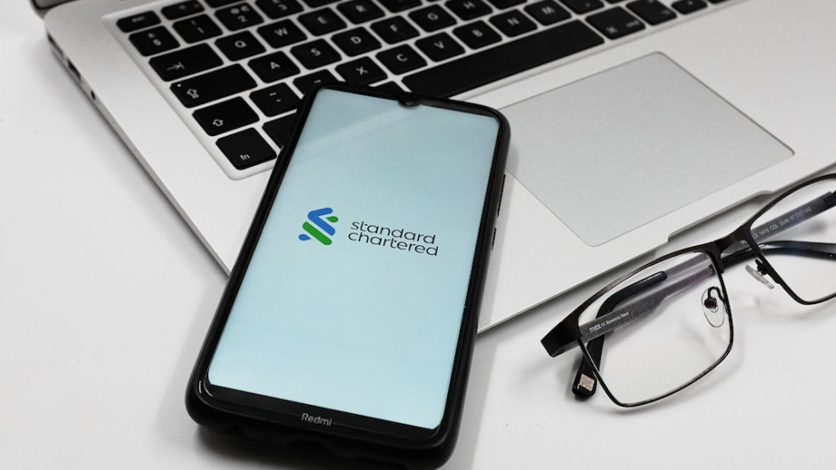 A Standard Chartered bank logo is displayed on a smartphone screen. Nikolas Kokovlis/NurPhoto via AFP