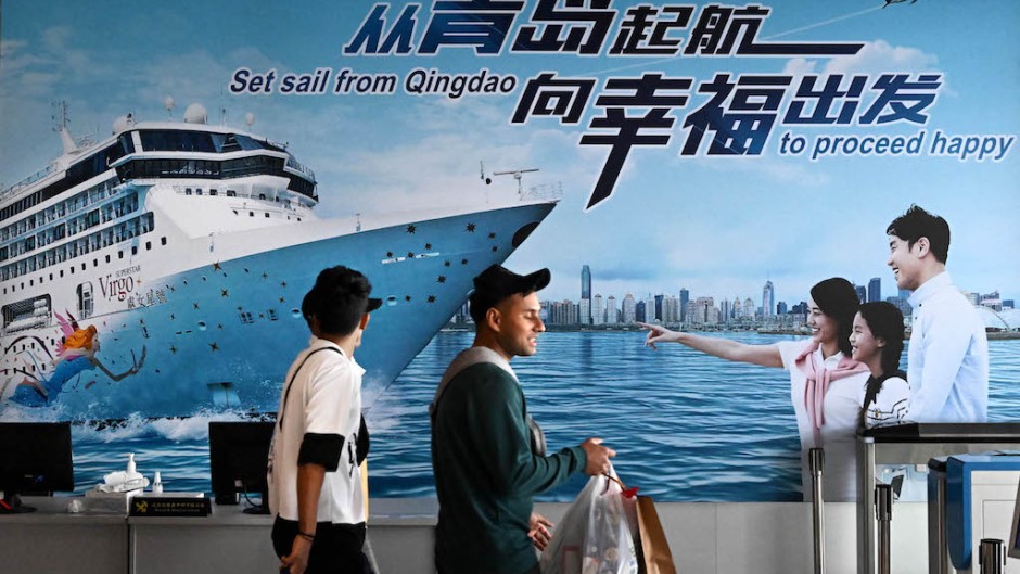 People walk past a billboard at the passenger transportation center of Qingdao Cruise Terminal in Qingdao. Li Ziheng/Xinhua via AFP