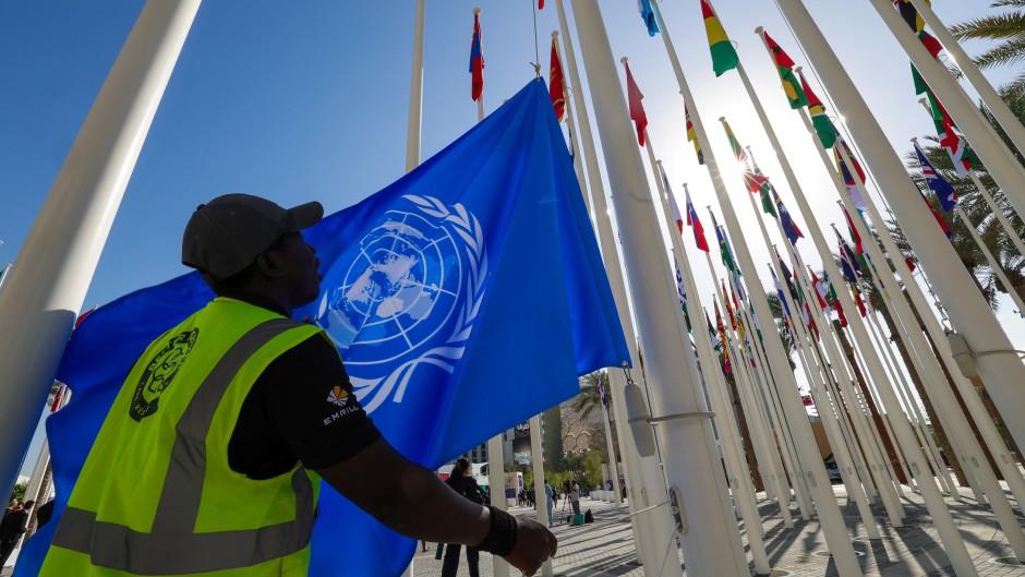 A worker prepares to hoist a United Nations flag with other national flags of participating countries at the venue of the COP28 UN climate summit in Dubai on November 30, 2023. The UN climate conference opens in Dubai on November 30 with nations under pressure to increase the urgency of action on global warming and wean off fossil fuels, amid intense scrutiny of oil-rich hosts UAE.