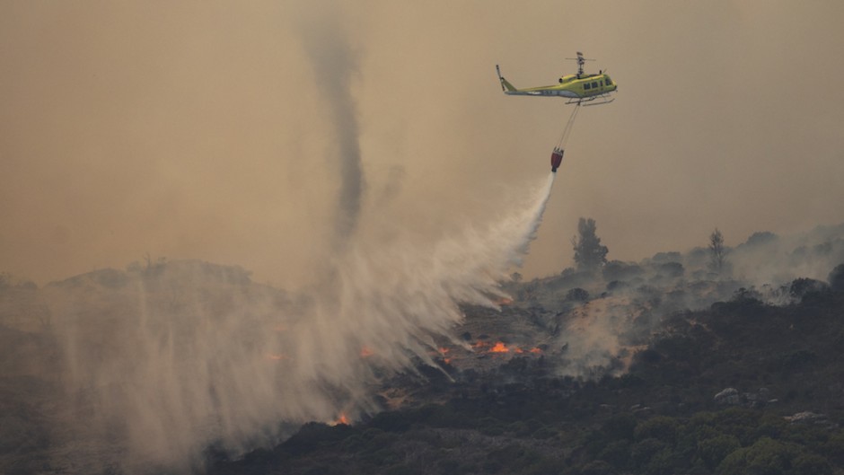 A Fire and Rescue helicopter water bombs a line of wildfire above the residential neighbourhood of Glencairn. AFP/Gianluigi Guercia