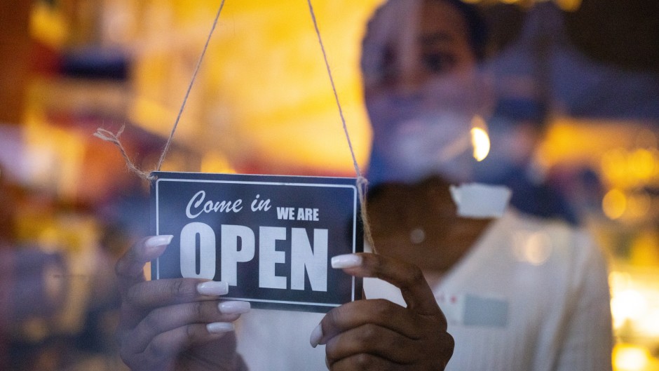 File: A woman turning an open sign on glass front door of a coffee shop. Getty Images/Luis Alvarez