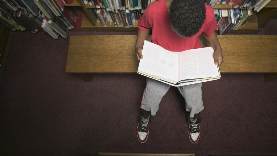 File: A young boy reading a book in a library. GettyImages/Andersen Ross Photography Inc