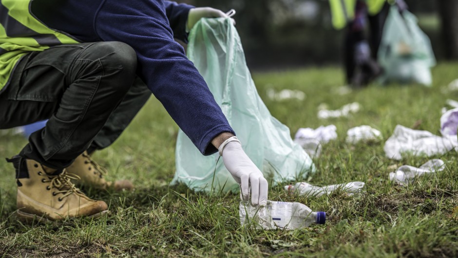 File: A volunteer picking up a plastic bottle during a park clean-up action. GettyImages/vm