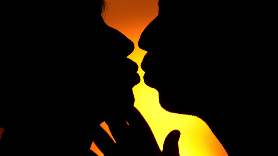 File: An illustrated picture shows a man and a woman kissing in front of the sunset.