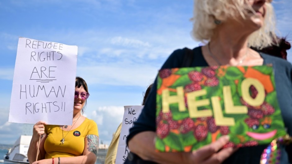 People hold up placards to welcome migrants to the barge which the government insists is a cost-effective option