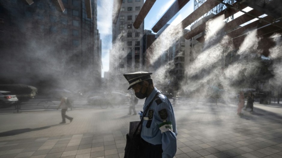 A security guard walks past an overhead water misting system on a hot day in Tokyo on July 10, 2023