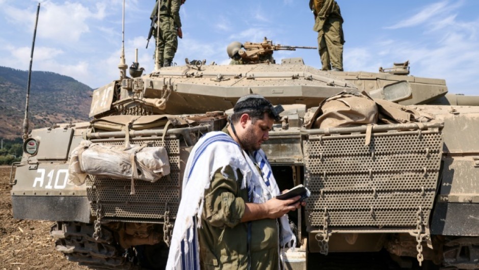 An Israeli soldier prays in front of a Merkava tank near the the northern town of Kiryat Shmona, close to the border with Lebanon, on October 8, 2023