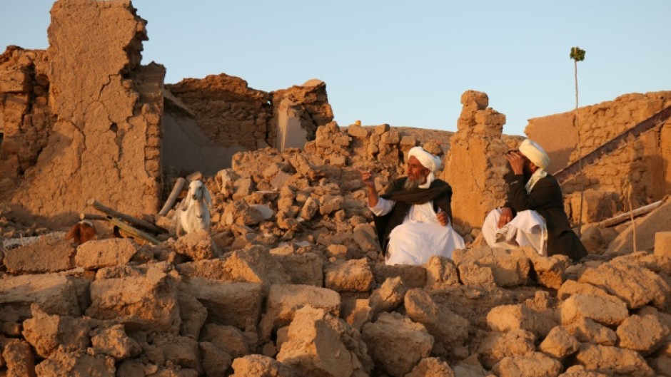 Afghan men sit in the rubble of their flattened homes in Sarbuland village in Herat province following Saturday's earthquake