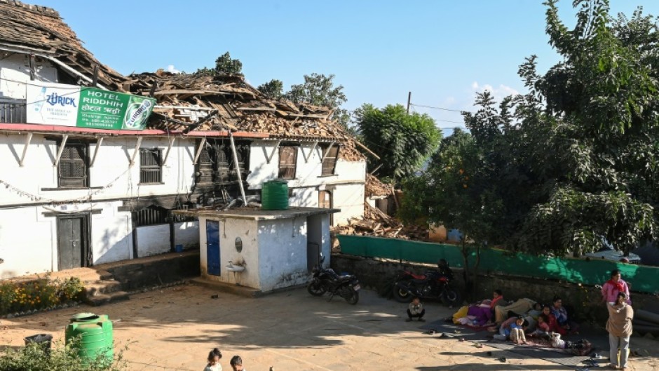 People rest outside next to a quake-damaged building in Jajarkot district