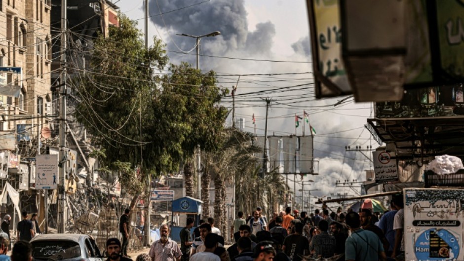 People walk along a street as a plume of smoke rises in the background during a strike on the Bureij refugee camp in the central Gaza Strip on November 2, 2023