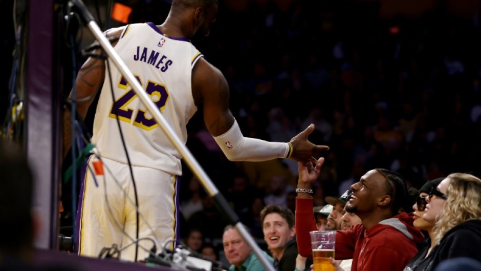 Bronny James, shown at right greeting his father LeBron during an NBA game on November 19, has been given medical approval to return to college basketball after suffering cardiac arrest during a July practice session, his family announced