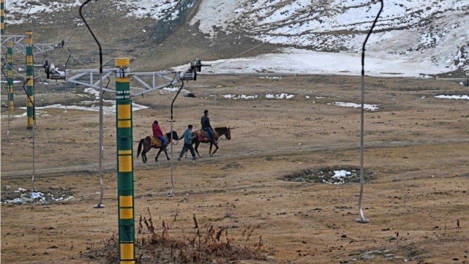 A guide leads horses along a path near ski slopes usually covered in snow in Gulmarg 