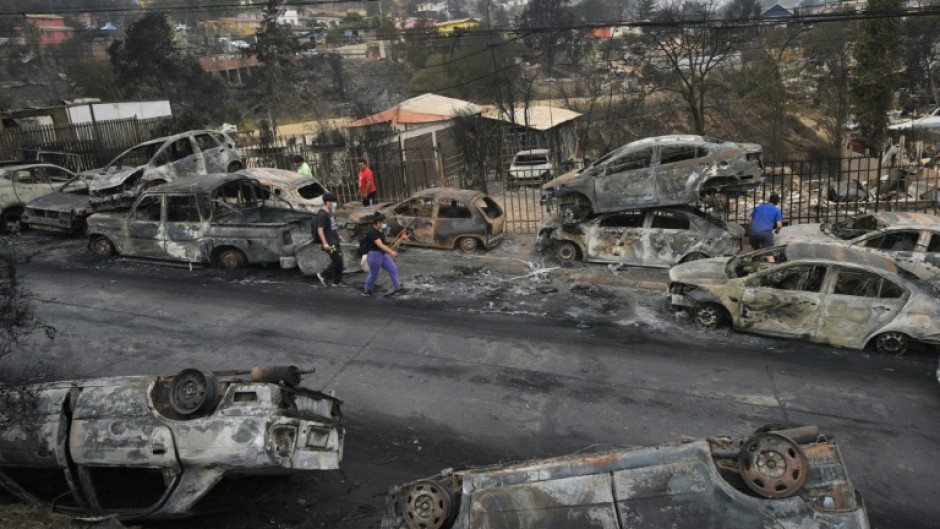 Survivors walk past burned out vehicles after a wildfire ravaged Quilpue, in Chile's Vina del Mar region