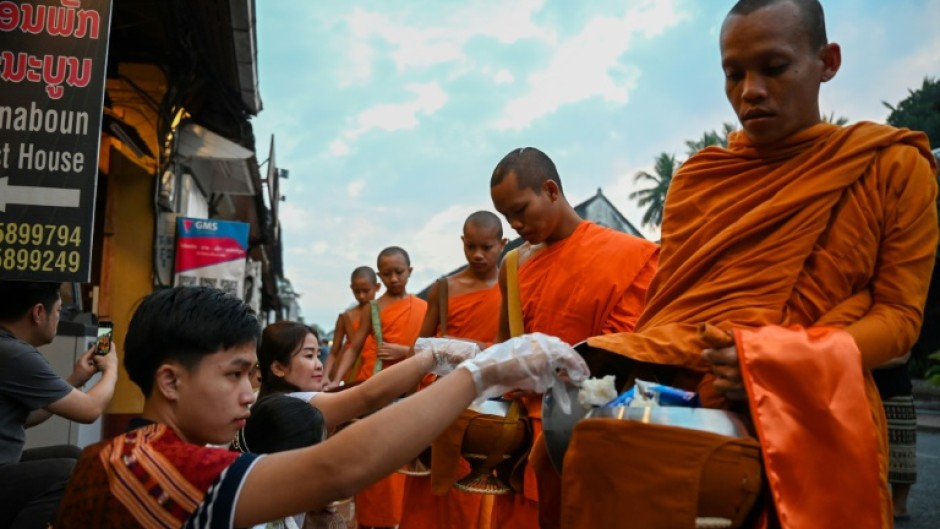 Monks have to make their way through hundreds of visitors on plastic stools offering alms as tour guides thrust mobile phones into their faces