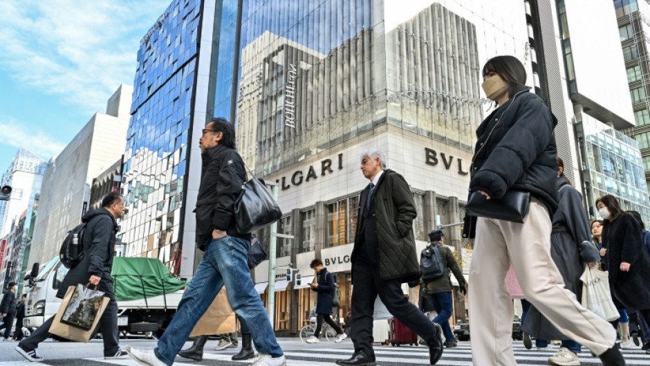 Pedestrians cross the street in front of luxury shops in the Ginza shopping district in Tokyo on January 19, 2024