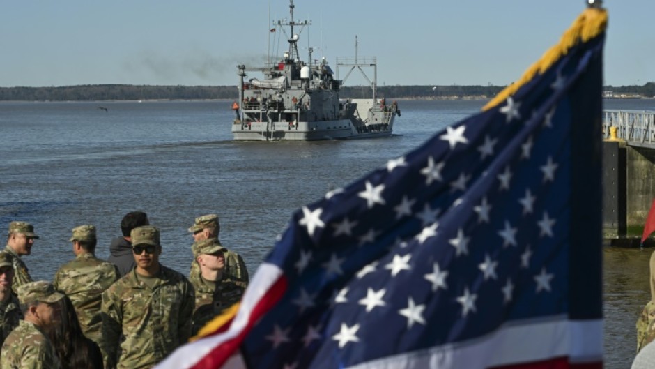 US Army soldiers stand near an American flag as the USAV Wilson Wharf departs on March 12, 2024 for an operation to construct a temporary port on Gaza's coast for the delivery of urgently needed aid