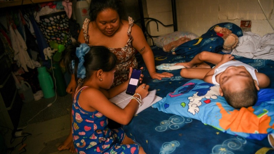 Cindella Manabat (C) helps her daughter Ella Araza (L) with homework, at their house in Manila 