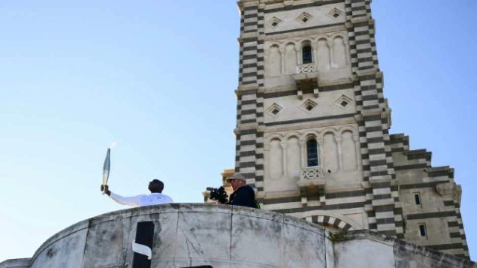 Basile Boli holds the Olympic torch aloft in front of the basilica of Notre-Dame de la Garde in Marseille