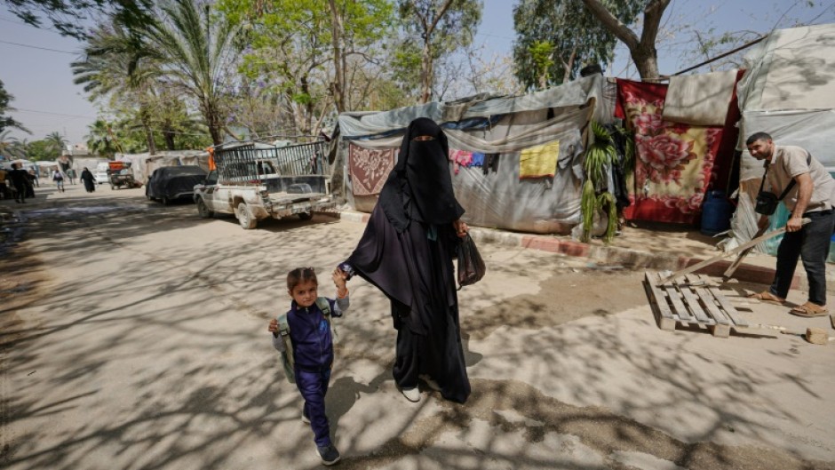 A displaced Palestinian woman holds a child by the hand as she walks in front of tents set up inside the European hospital compound in Khan Yunis in the southern Gaza Strip