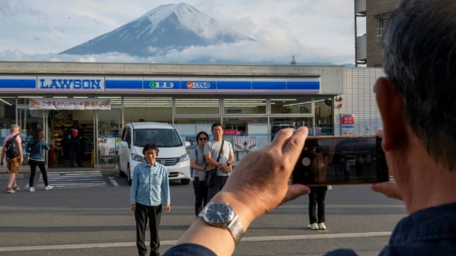 Tourists take pictures of Mount Fuji from opposite a convenience store in the town of Fujikawaguchiko, Yamanashi prefecture