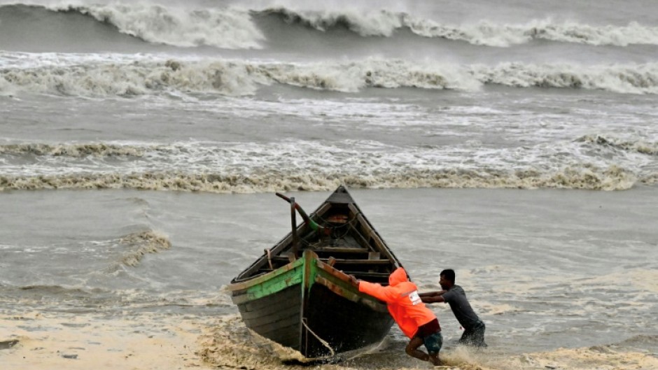 Men push a fishing boat to a sea shore as a preventive measure during rainfall in Kuakata on May 26, 2024, ahead of cyclone Remal's landfall in Bangladesh