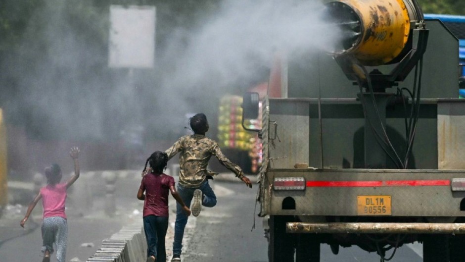 Children run behind a truck spraying water along a street on a hot summer day in New Delhi on Tuesday