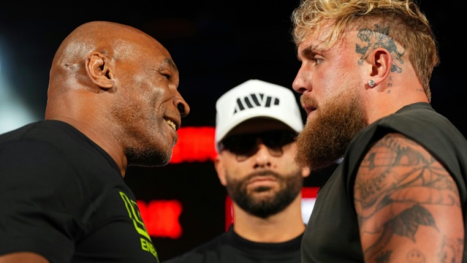 Mike Tyson, left, and Jake Paul, right, stare at each other while promoter Nakisa Bidarian, center, looks on ahead of their heavyweight boxing showdown, which has been rescheduled for November 15