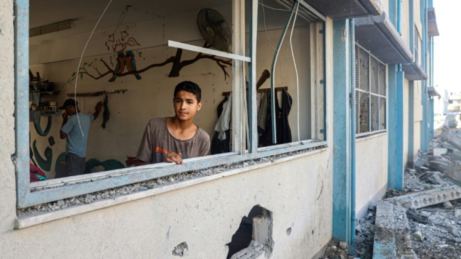 A Palestinian boy stands by a shattered window at a UN school sheltering displaced people which was damaged during Israeli bombardment in Khan Yunis, southern Gaza