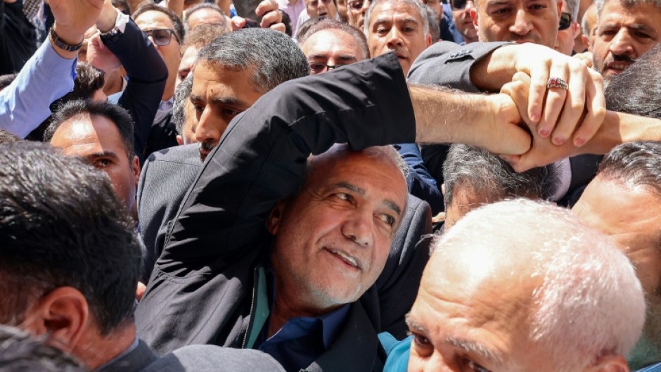 Iranian reformist presidential candidate Masoud Pezeshkian (C) greets supporters outside a polling station in Tehran during the runoff