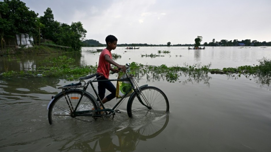 A boy pushes his bicycle through a flooded part of Jhargaon village in Morigaon district, Assam