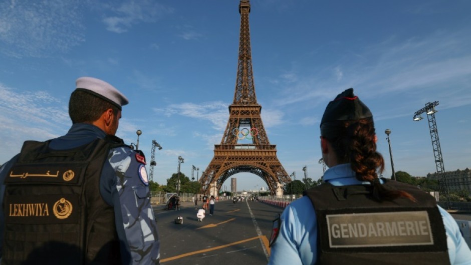 A French policewoman and a Qatari policeman stand guard near the Eiffel Tower as security preparations step up for the Paris Olympics