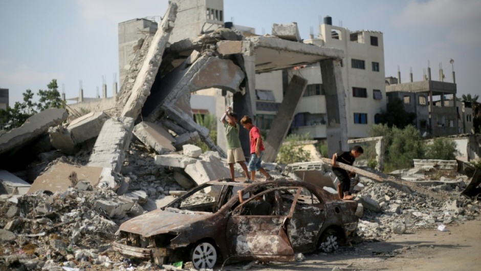 Palestinian children play on the wreckage of a car near a building destroyed in Israeli bombardment, in central Gaza's Al-Bureij refugee camp