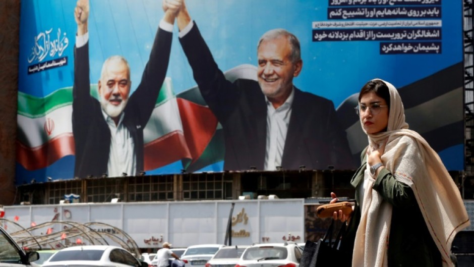 A woman walks past a picture of Iranian President Masoud Pezeshkian (R) and slain Hamas leader Ismail Haniyeh in Tehran