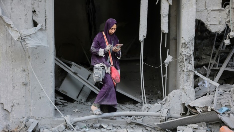 A woman checks her phone amid the rubble of a building destroyed by Israeli bombardment in Gaza City's Sheikh Radwan district