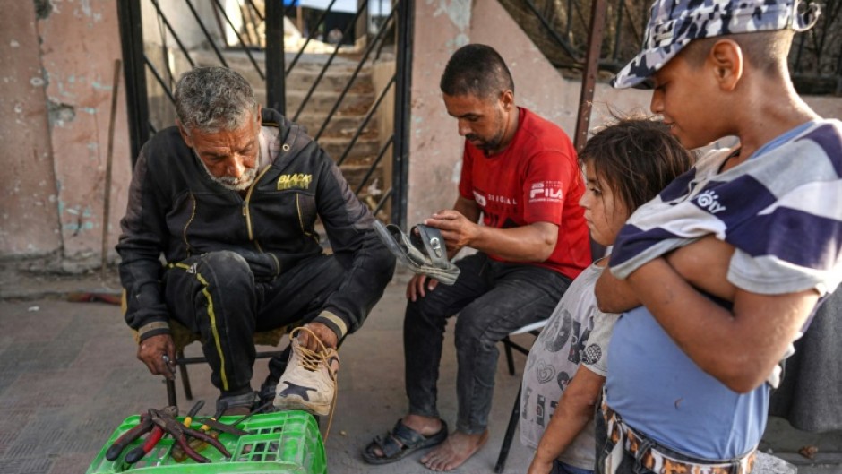 Palestinians wait for a cobbler to repair their shoes in Khan Yunis in the southern Gaza Strip