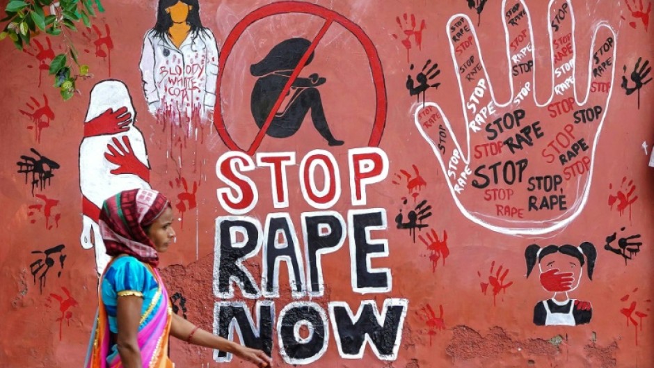 A woman walks past a mural painted on a wall in Ajmer condemning the rape and murder of a doctor in India's West Bengal state