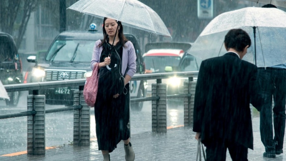 People carrying umbrellas walk across a street in Tokyo on August 30. Typhoon Shanshan weakened to a tropical storm but was still dumping heavy rains as it slowly churned through Japan