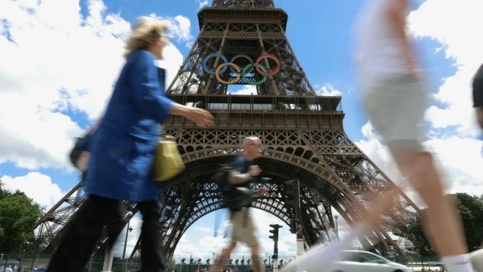 Pedestrians walk past the Eiffel Tower adorned with the Olympic Rings ahead of the 2024 Olympic Games in Paris in July 16, 2024.