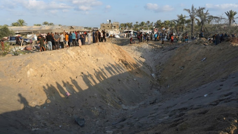 Palestinians stand on the edge of a crater in the Al-Mawasi displacement camp in the Gaza Strip