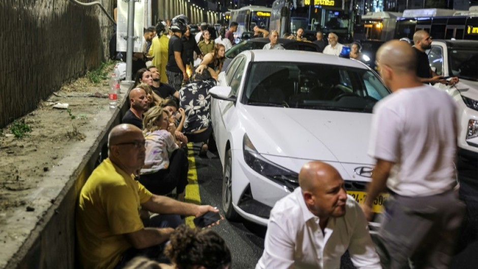 People take cover behind vehicles under a bridge in Tel Aviv after air raid sirens sound